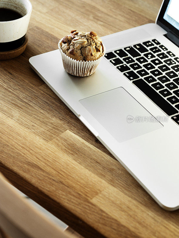 笔记本电脑和纸杯蛋糕放在木桌上，一边工作一边享受甜食