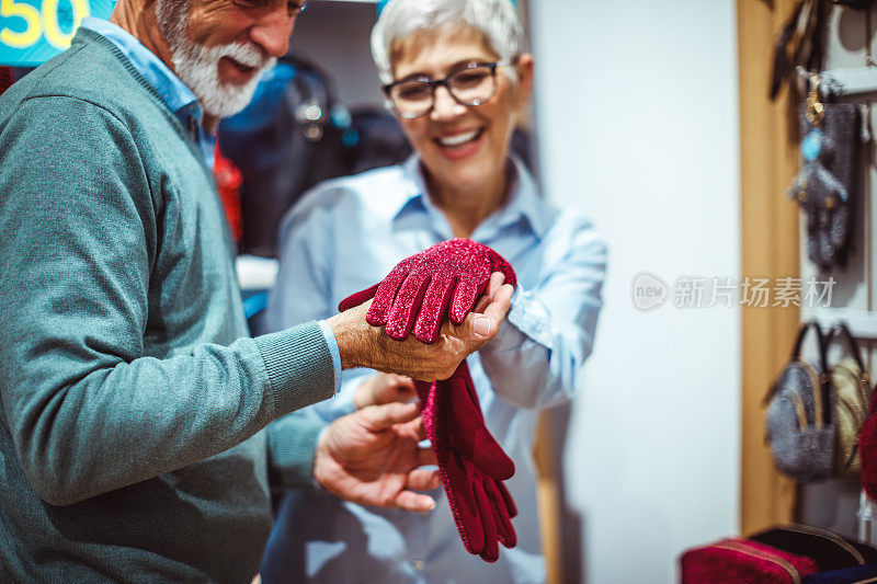 在一家手提包商店里，一位老年妇女向她的伴侣展示一双鲜红的手套