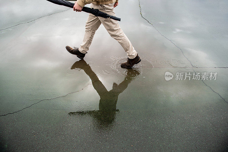 一名男子撑着伞在潮湿的柏油路上行走