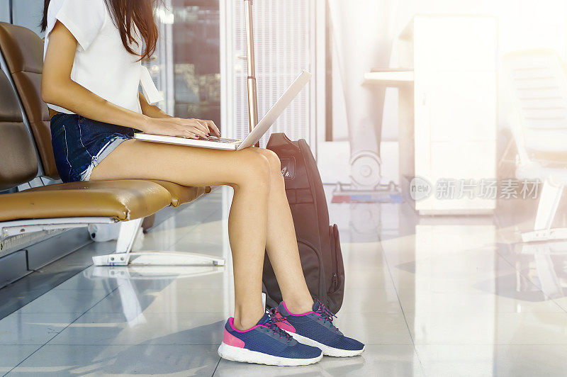 一名年轻女子在机场用平板电脑等待飞机。她正推着旅行箱手推车坐着。