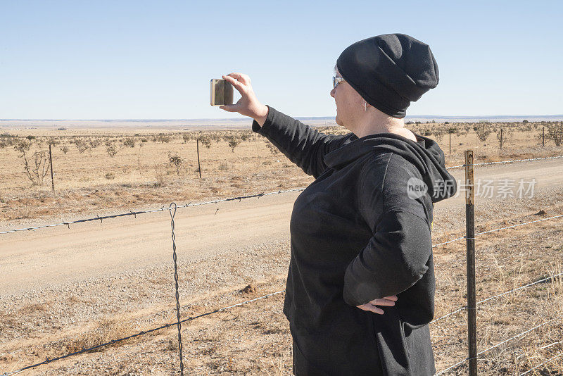 旅行的记忆。一位成熟的女性，一名游客，在新墨西哥州的公路旅行中用智能手机拍下了沙漠的风景