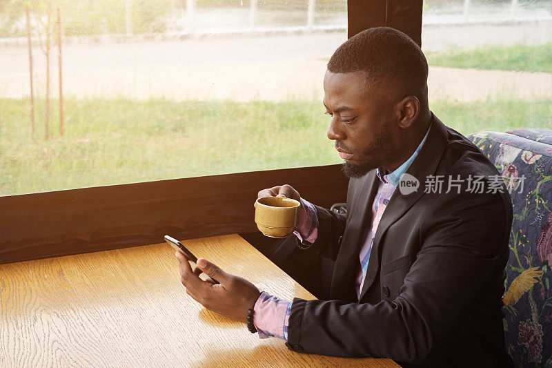 非裔美国商人坐在咖啡馆里用智能手机输入信息。