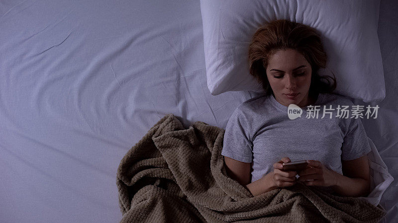 睡觉前躺在床上用智能手机上网的女人