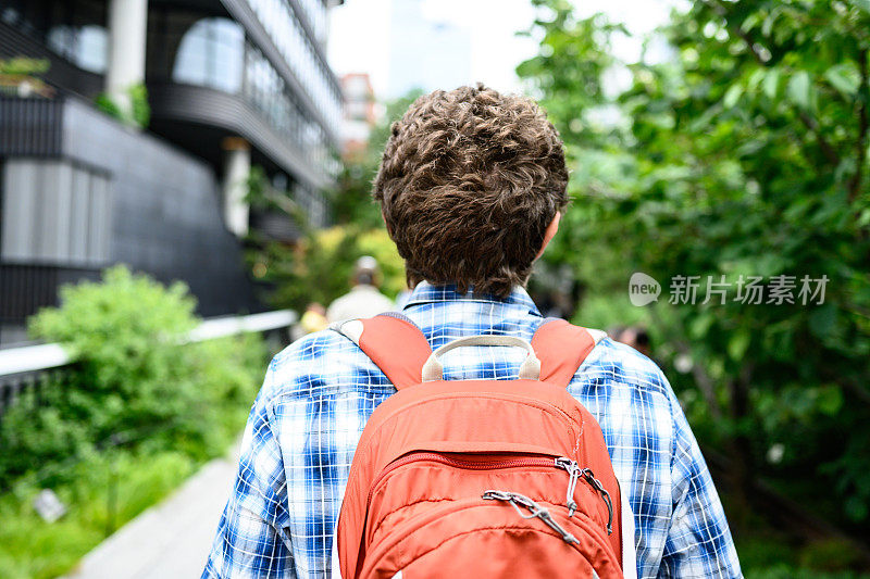 在纽约高架线上背着背包行走的30岁白人男子的后视图