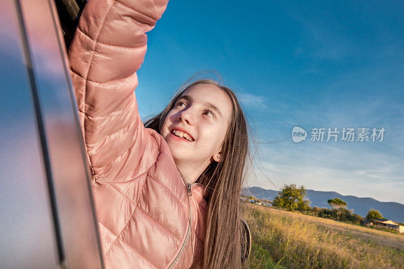 可爱的女孩探出车窗，双臂向上享受秋天的公路旅行