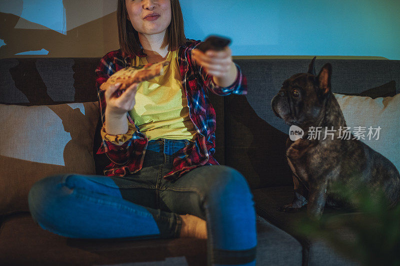 一个女人在沙发上吃披萨，和她的狗一起看电视