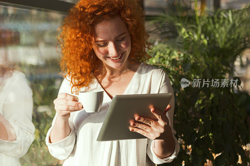 漂亮的红发年轻女子在咖啡厅使用电子平板电脑