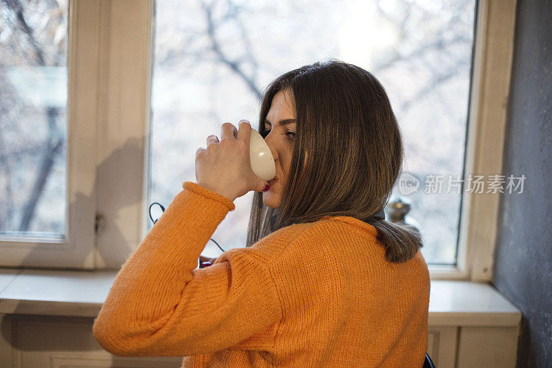 美丽的年轻女子，早上在窗边喝咖啡