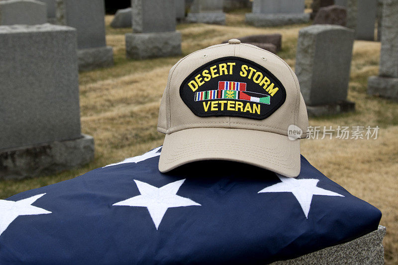 沙漠风暴老兵的帽子坐在一个墓地的墓碑上的美国国旗上。
