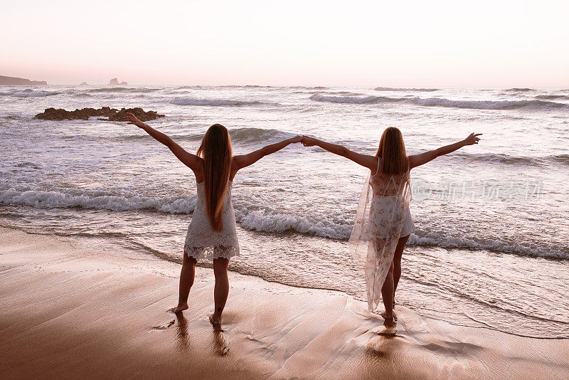 两名年轻女子在海滩上举起手臂