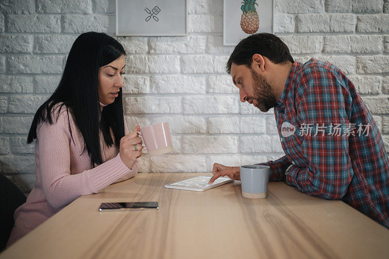 一对年轻夫妇在餐厅里用平板电脑一边喝咖啡一边看新闻
