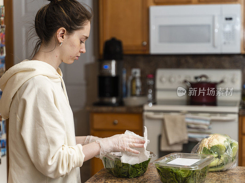 一名年轻女子用湿消毒湿巾清洁食品杂货，以防止COVID-19大流行造成污染。