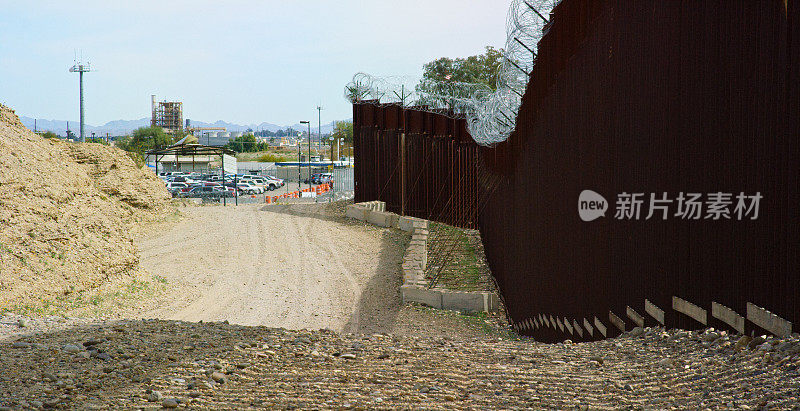 一条土路，美国海关和边境巡逻队，墨西哥和美国之间的钢条边境墙，上面有铁丝网，在一个晴朗、阳光明媚的日子里