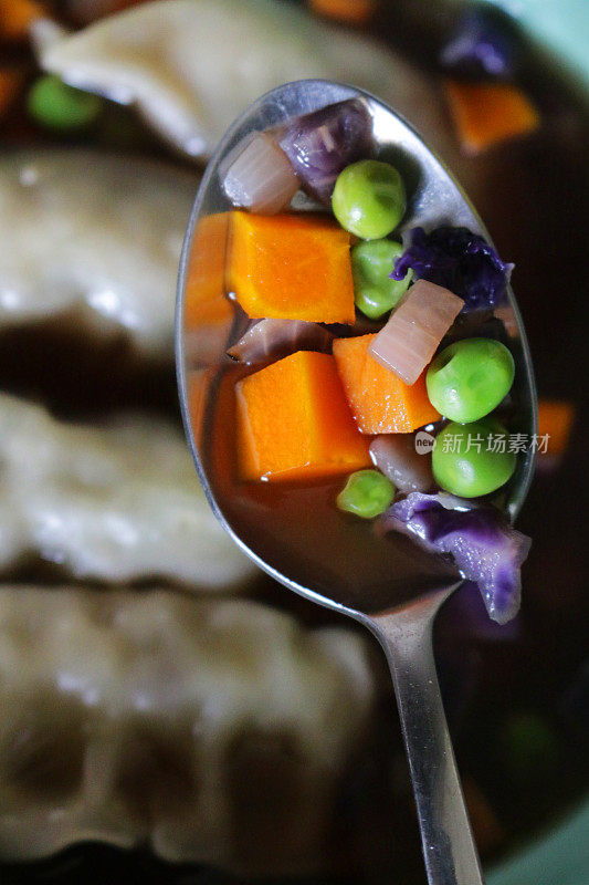 这是一碗由鸡肉馄饨和蔬菜汤组成的汤碗，一碗由胡萝卜、豌豆和中国饺子组成的亚洲蔬菜汤