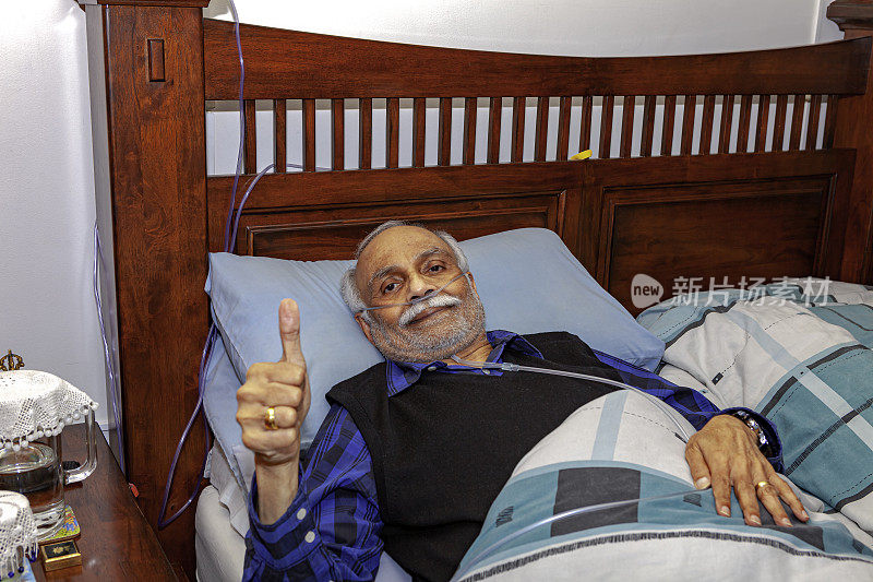 一名72岁的印度男子做完腹腔镜胆囊手术后躺在家中的床上恢复。他对着镜头竖起大拇指，表示他做得很好。