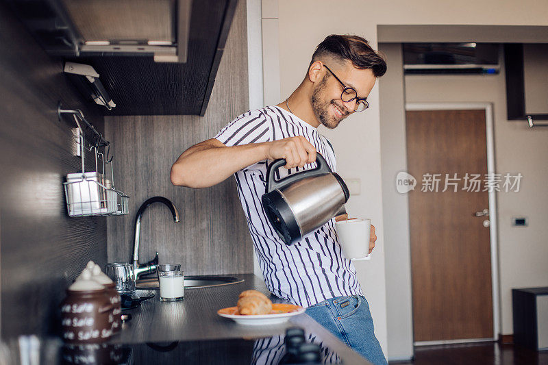 快乐的年轻人享受他的早晨，准备咖啡和早餐