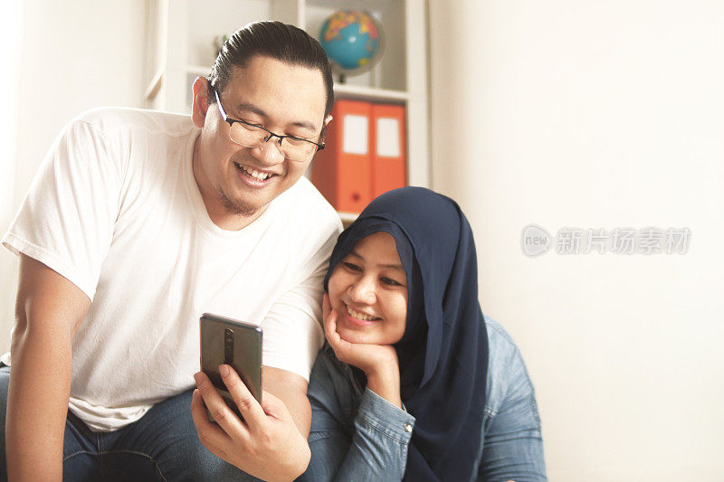 亚洲穆斯林夫妇在看智能手机时笑得很开心，网上有好消息