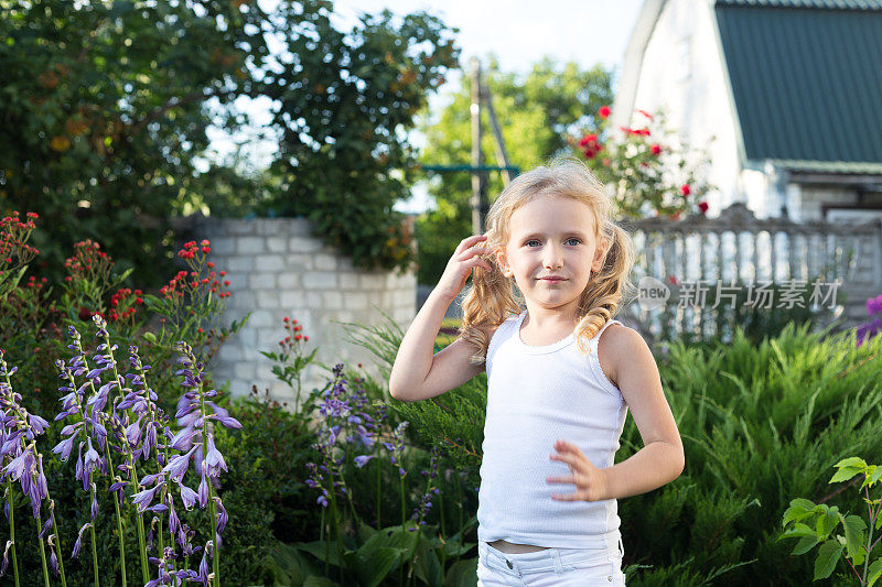 一个小女孩在房子院子里的花园里带着花散步。