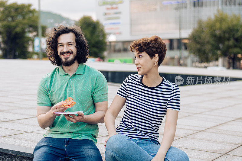 一个年轻人和他的女朋友在街上吃披萨休息