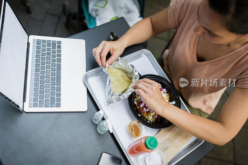 年轻女子在户外餐厅吃午饭，而她的孩子睡在婴儿车里。