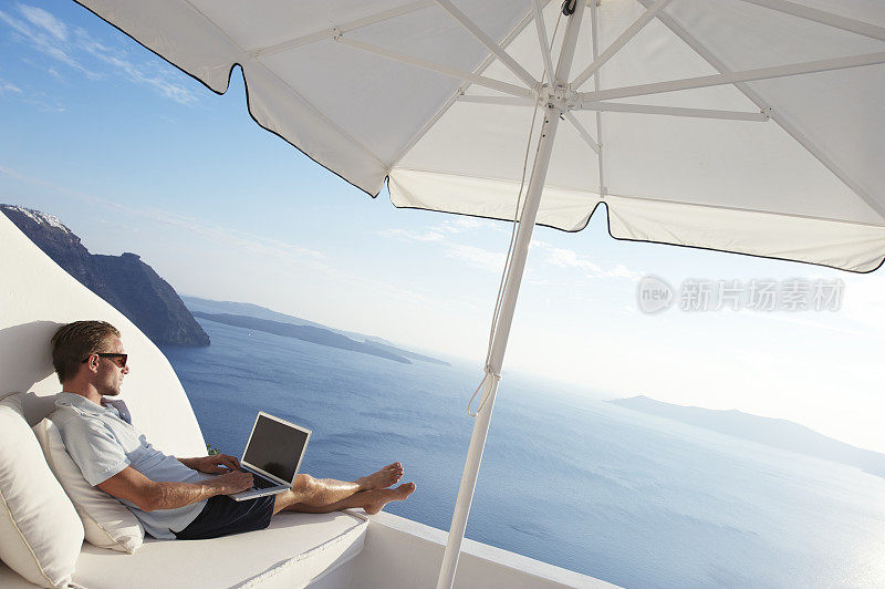 男士放松豪华阳台与笔记本电脑地中海岛的看法
