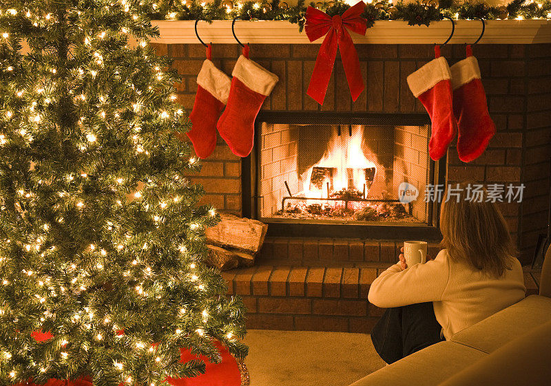 一个女人坐在圣诞树旁，壁炉里炉火熊熊