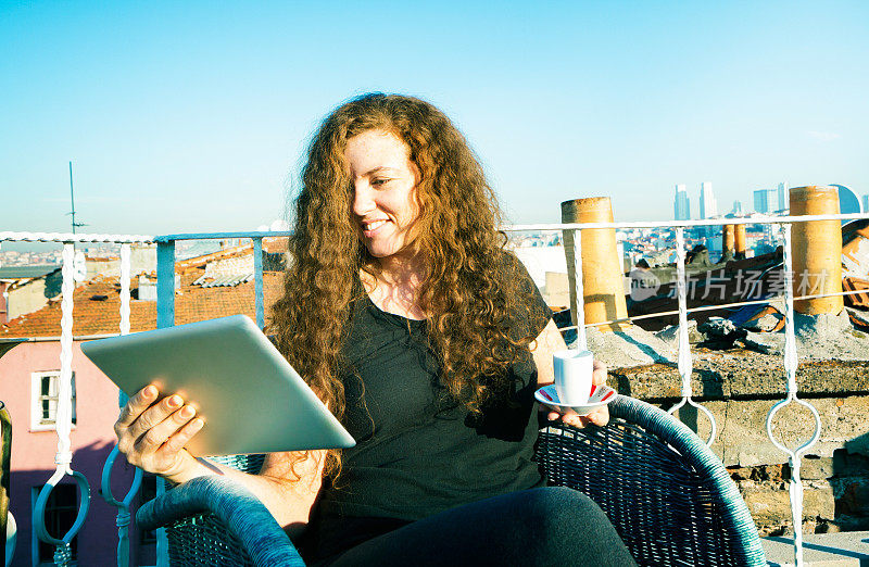 红发女人在屋顶上喝着咖啡喝着平板电脑