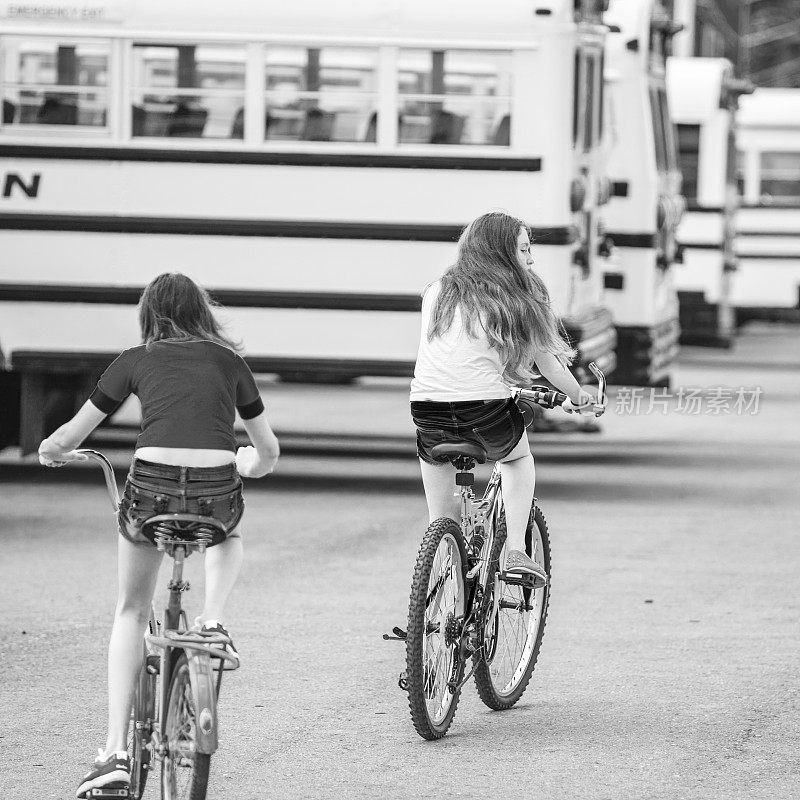 两个女孩在校车旁边骑车
