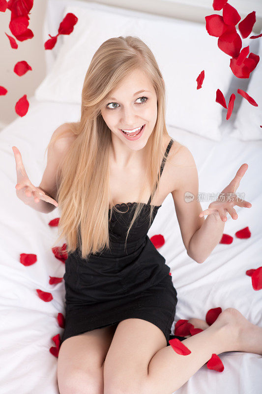 美丽的年轻女子把玫瑰花瓣撒在床上