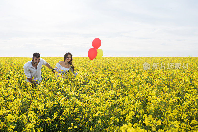 一对无忧无虑的夫妇带着气球在满是春花的草地上奔跑。