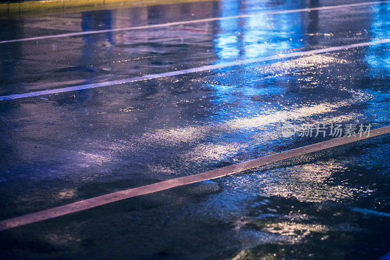 五颜六色的灯光在雨中潮湿的沥青上反射