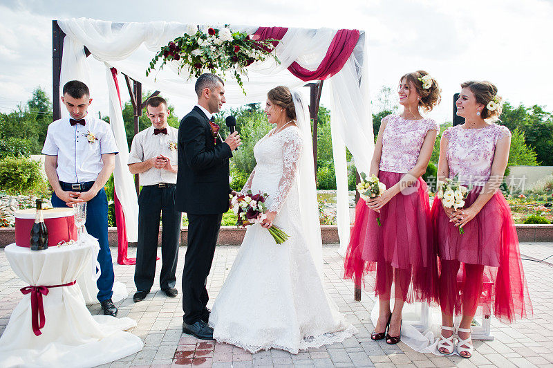 婚礼新人在众多宾客面前，在户外的花艺拱门下宣誓。
