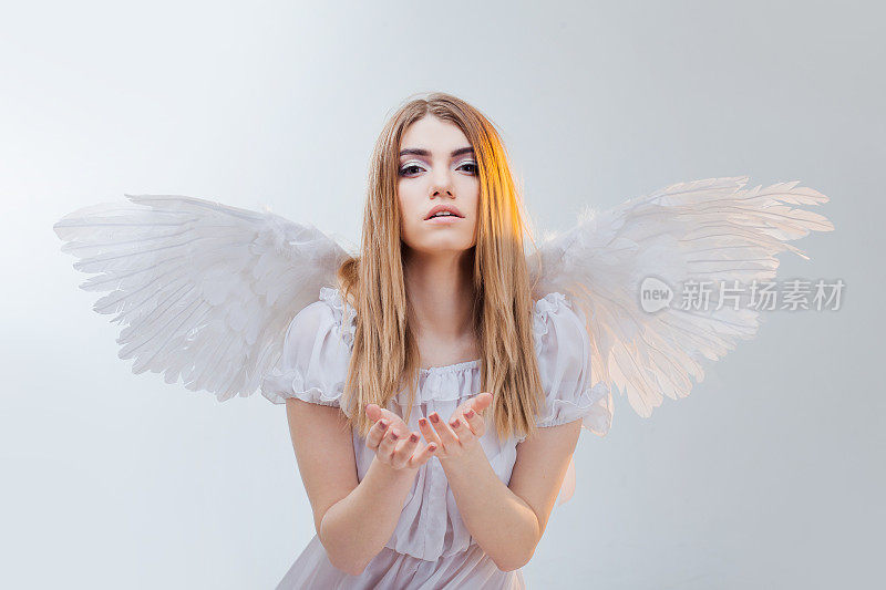 一个来自天堂的天使，手里拿着什么东西。年轻漂亮的金发女孩，就像长着白色翅膀的天使。