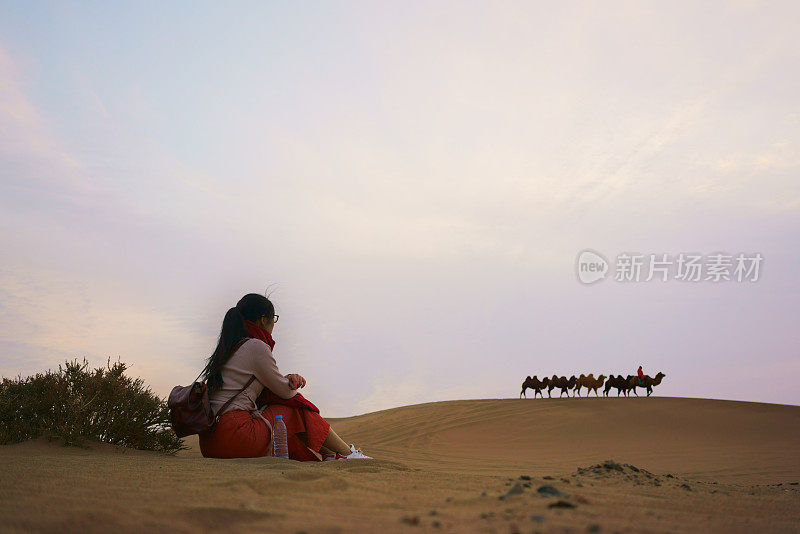 在沙漠日出时，女人在沙丘上放松