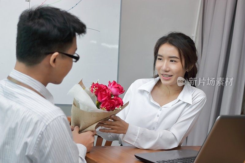 快乐的年轻亚洲女子在情人节从办公室的男朋友那里接受了一束红玫瑰。职场爱情和浪漫的概念。