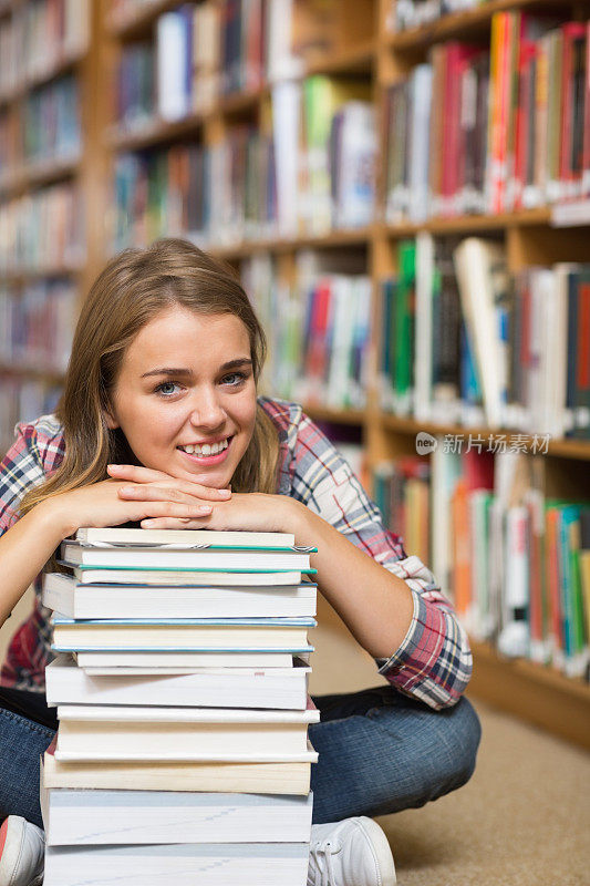 快乐的学生坐在图书馆的地板上倚着一堆书