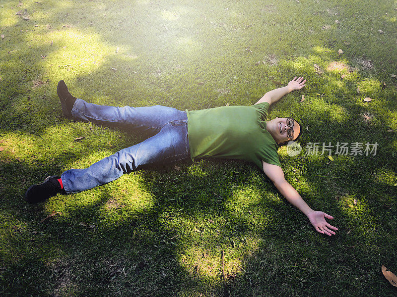 日本人在夏日的阳光下，张开双臂躺在绿色的草地上。