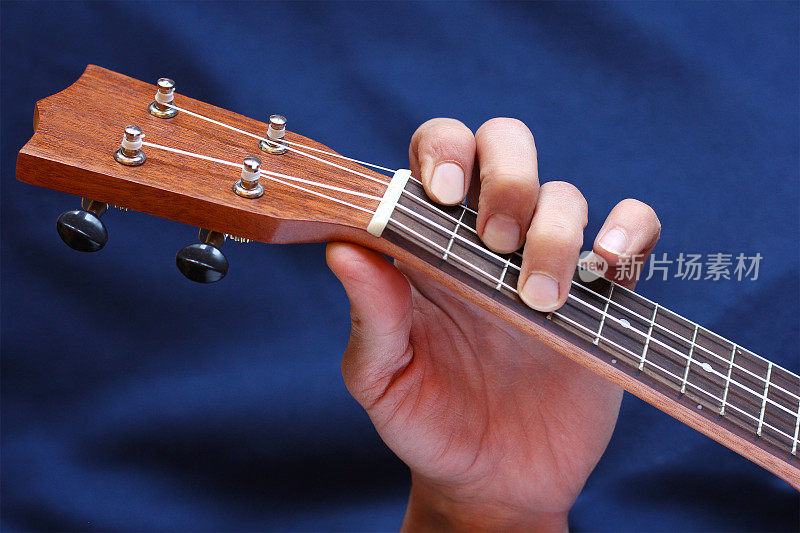 左音乐家的手夹在四弦琴上的和弦，侧视图