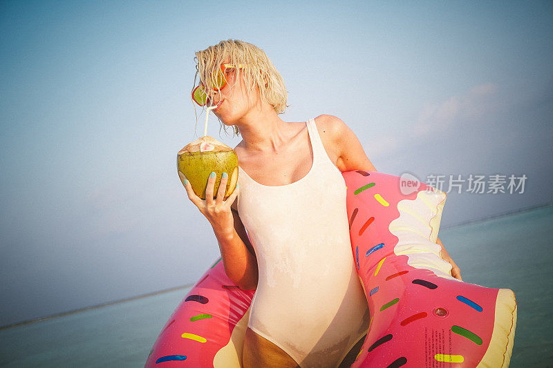 金发女子站在马尔代夫的海边喝椰子水