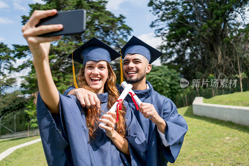 一对刚从大学毕业的情侣用智能手机自拍，一名男子拥抱了一名女子，两人都笑着