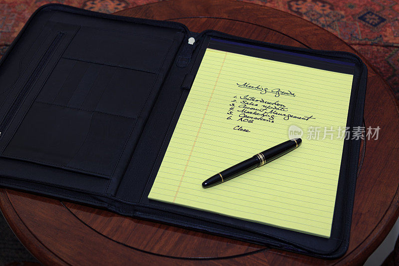 在黄色便笺本上手写的会议议程，装在皮包里，放在红木桌上，还有雅致的钢笔。副本的空间。