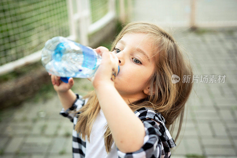 美丽的小女孩正在喝瓶子里的干净水。炎热的夏天