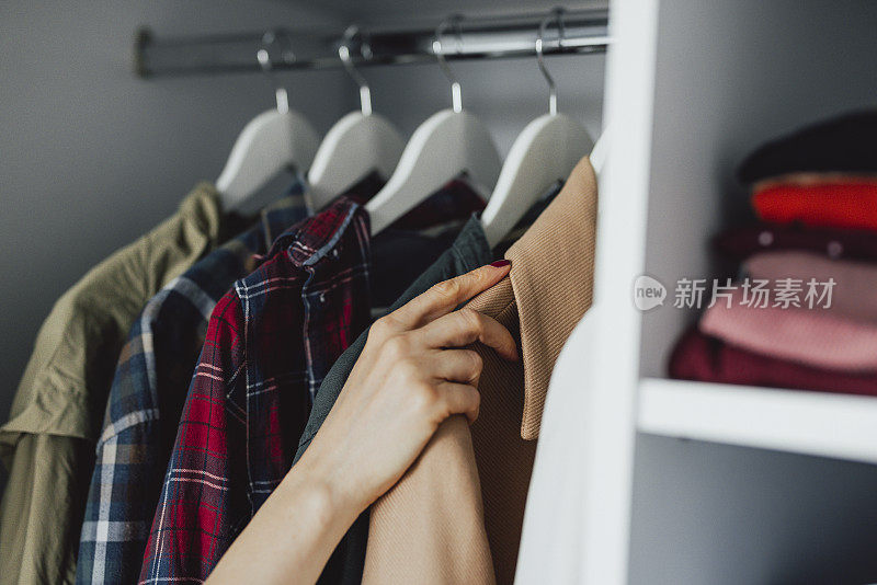 近距离照片的女人选择衣服在一个机架上在家里