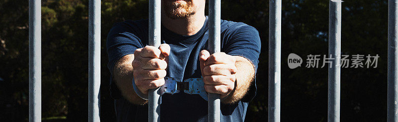 戴着手铐的男子紧握着监狱的栏杆