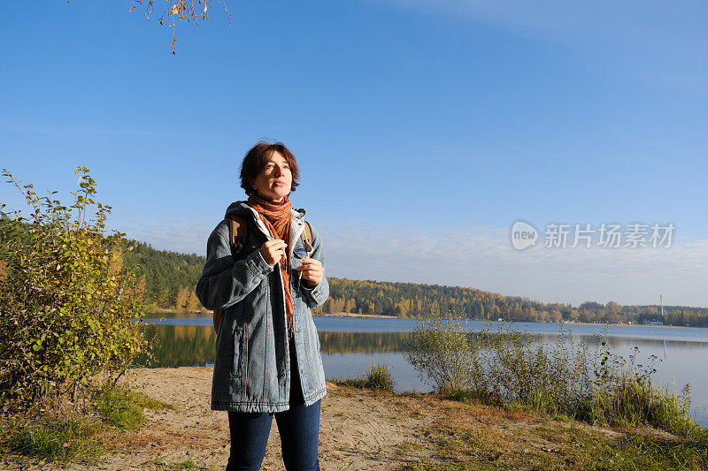 成熟的女人在阳光明媚的秋天自然公园的湖岸