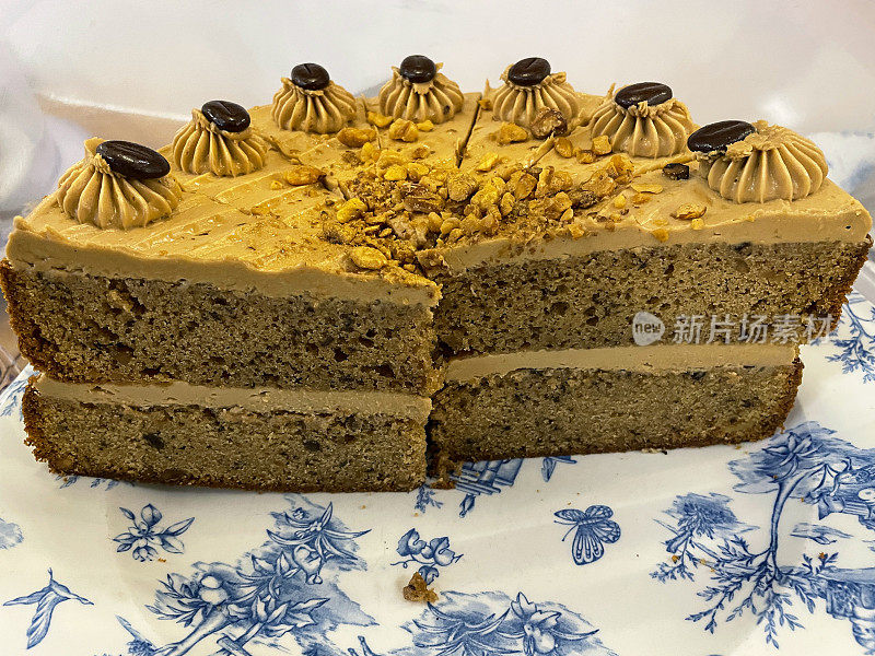 蓝色花卉图案的盘子展示切好的咖啡蛋糕，美味的甜点，覆盖着奶油，切碎的核桃和咖啡豆，高视野