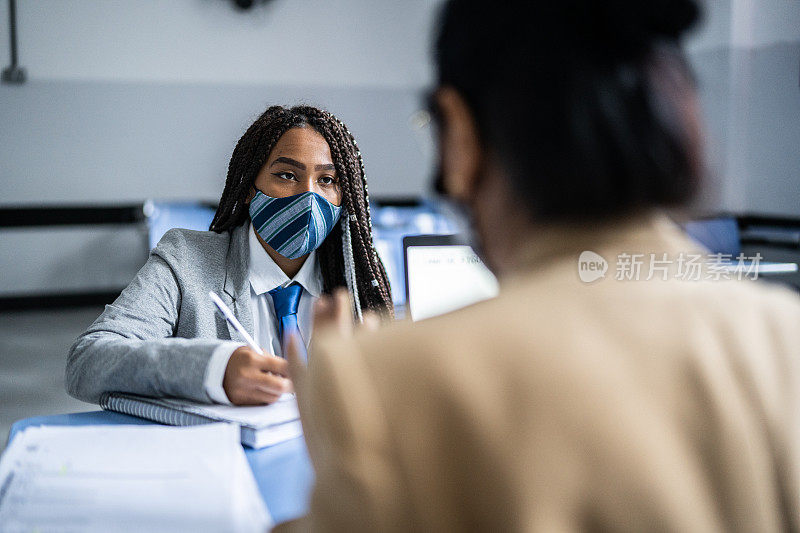 十几岁的学生在教室里和老师一起学习，戴着口罩