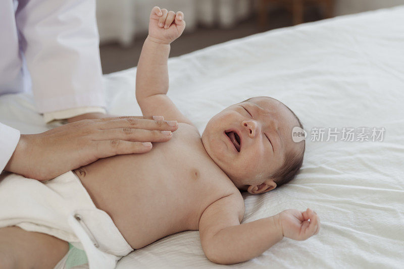 一名亚洲新生儿因生病住院，害怕医生检查，在床上哭泣。