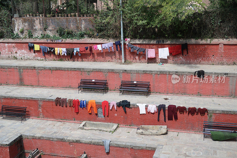 尼泊尔加德满都的一家公共洗衣店，墙上挂着晾衣绳和成排的衣服，在阳光下晒干