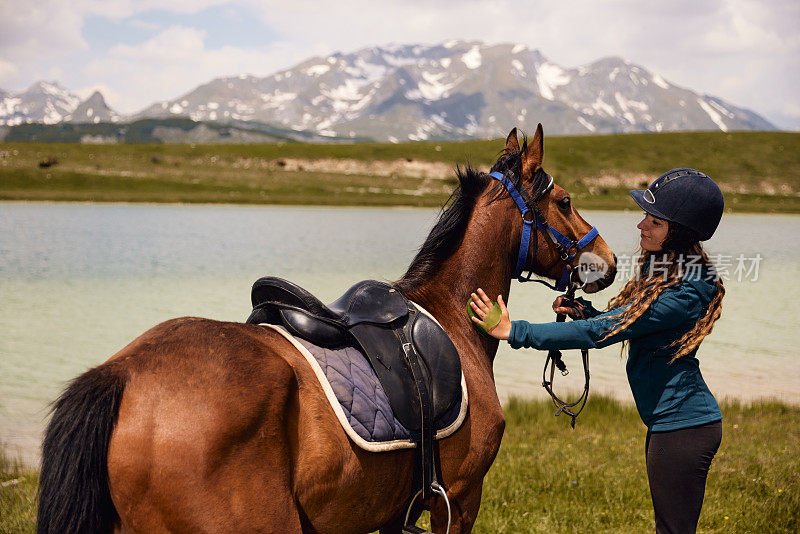 年轻女子在湖边骑马后正在给马梳洗